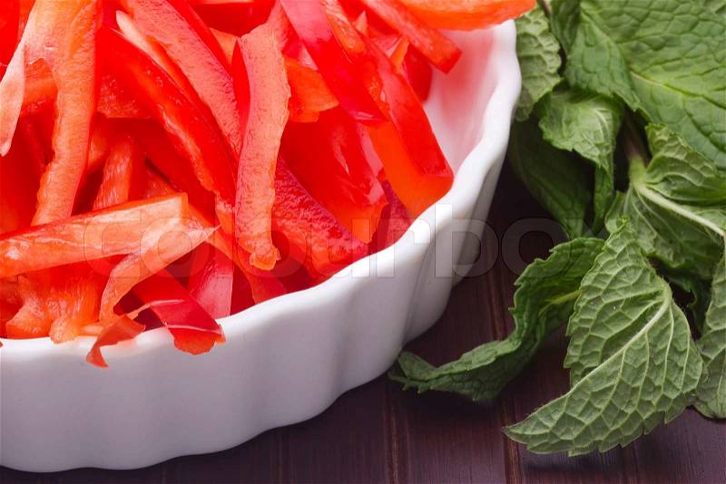 Image of 'Sliced red bell pepper in a white plate and green mint.'
