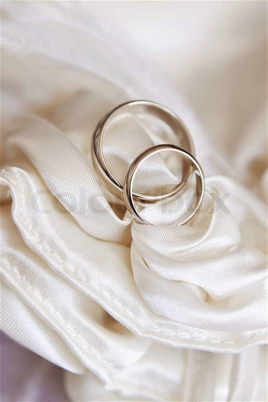 Stock image of 'wedding rings on white satin fabric'