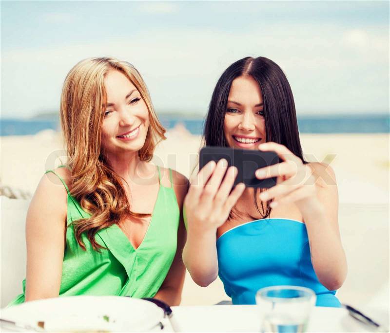Summer holidays, vacation and technology - girls taking photo with smartphone in cafe on the beach, stock photo