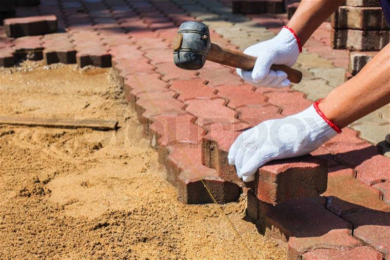 Worker laying red concrete paving blocks, stock photo