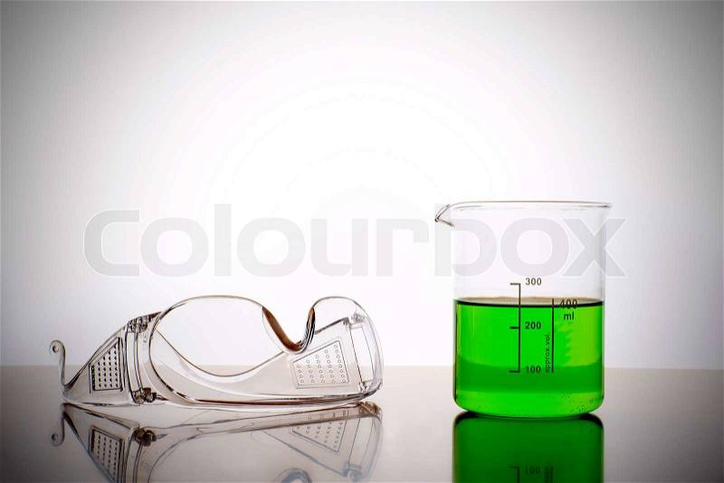 Measuring glass with green liquid and safety glasses, goggles in a chemical lab, stock photo