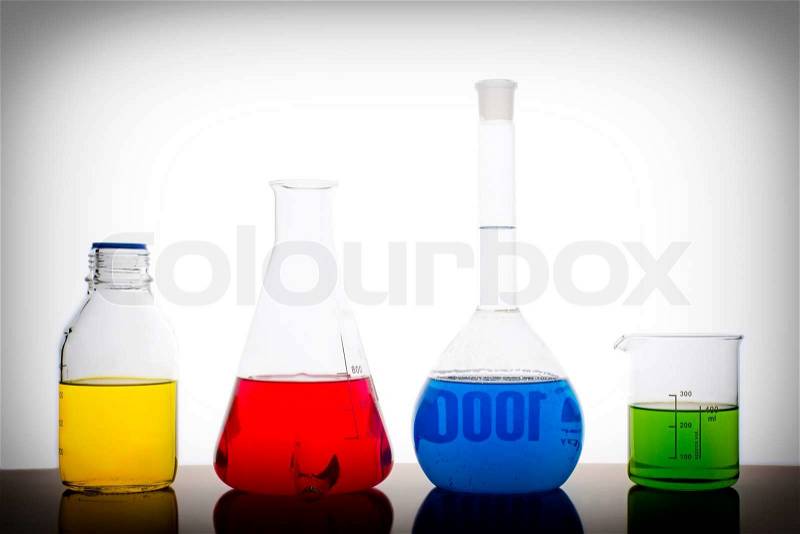 Four measuring glasses on a table of a chemical laboratory with red, yellow, blue and green liquid on white background, stock photo