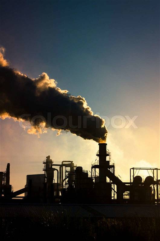 Smoking chimney at sunset on industrial buildings complex, stock photo