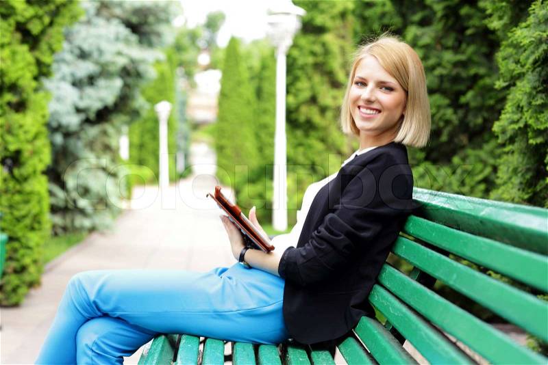 Happy woman sitting on the bench with tablet computer, stock photo