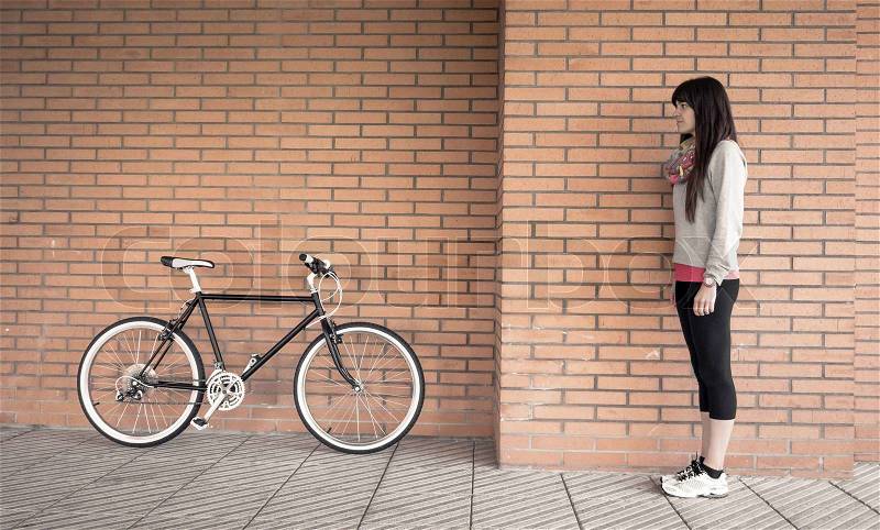 Beautiful young sportive woman posing with custom fixie bike over a orange brick wall on the background, stock photo