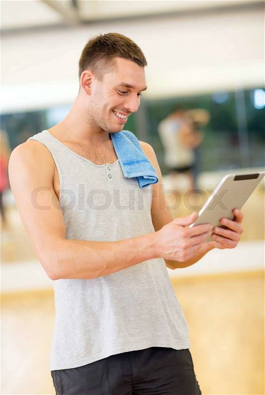 Fitness, sport, training, gym, technology and lifestyle concept - young man with tablet pc computer and towel in gym, stock photo