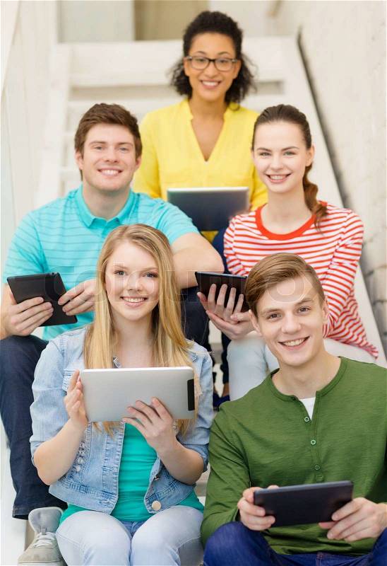 Education and technology concept - smiling students with tablet pc computer sitting on staircase, stock photo