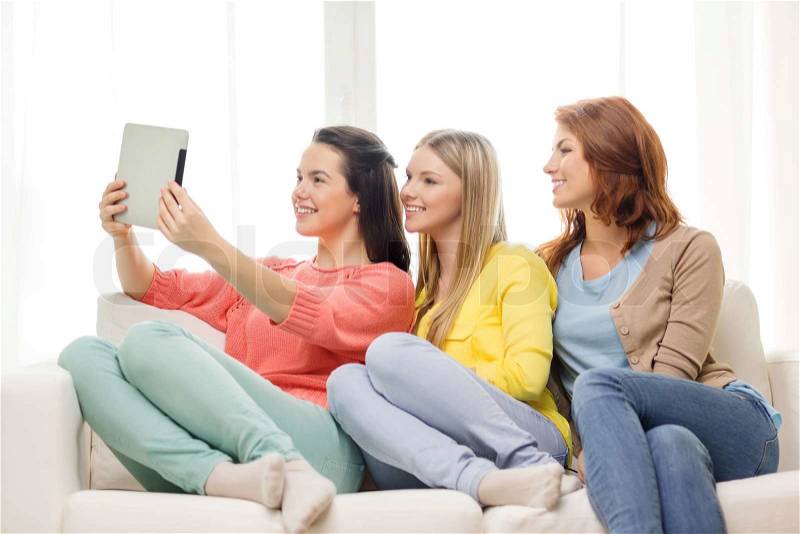 Friendship, technology and internet concept - three smiling teenage girls taking picture with tablet pc computer camera at home, stock photo