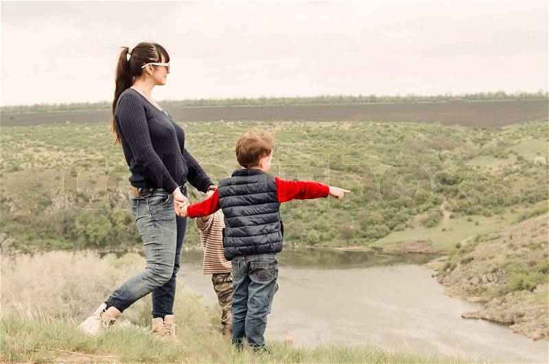 Little boy pointing to something in the countryside showing his mother a point of interest as they stand together on top of a grassy hill overlooking a steep valley and river, stock photo