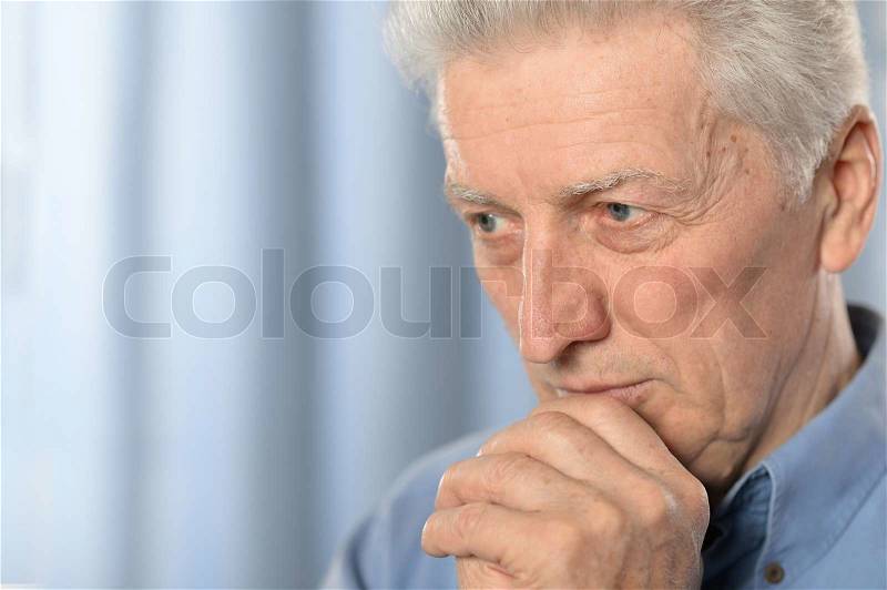 Cute older thoughtful man poses on blue background, stock photo