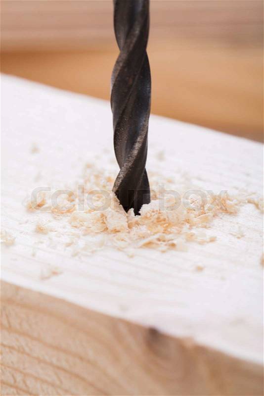 Battery operated hand drill standing amongst planks of new wood with a steel bit left protruding from a board in a concept of DIY, carpentry or joinery, stock photo