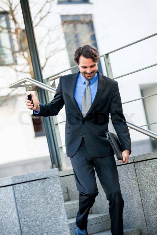 Smiling stylish young businessman walking down a flight of stairs in an outdoor urban setting holding a briefcase or folio in his hand, stock photo