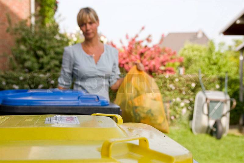 A caucasian mother throwing a waste bag in a recycling bin, stock photo
