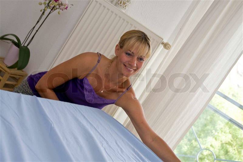 A smiling caucasian woman changing bed linen, stock photo