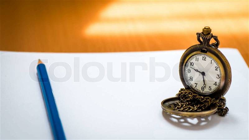 Open blank notebook with blue pencil and pocket watch on wood background with natural light, stock photo