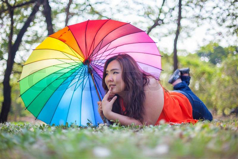Happy fatty asian woman with umbrella outdoor in a park, stock photo