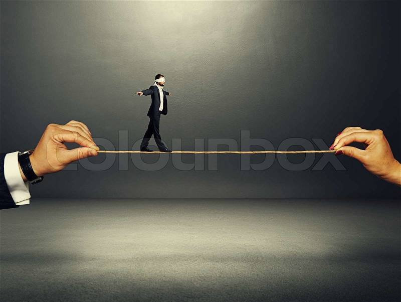 Man with the blindfold walking on the rope over dark background, stock photo