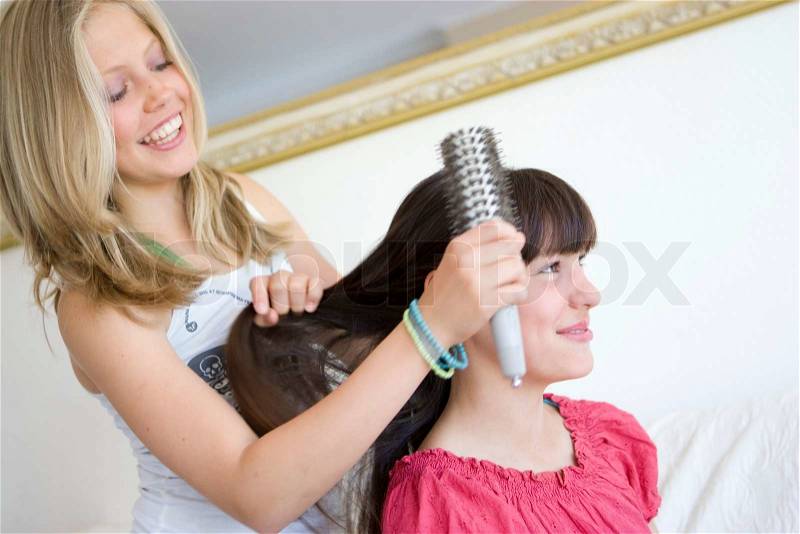 A teenage girl brushing the hair of her friend, stock photo