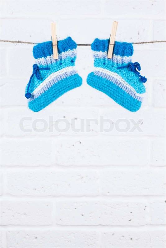 Knitted baby socks hanging on clothesline against white brick wall, stock photo
