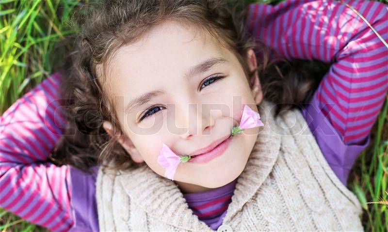Portrait of a funny little girl lying on the grass, stock photo