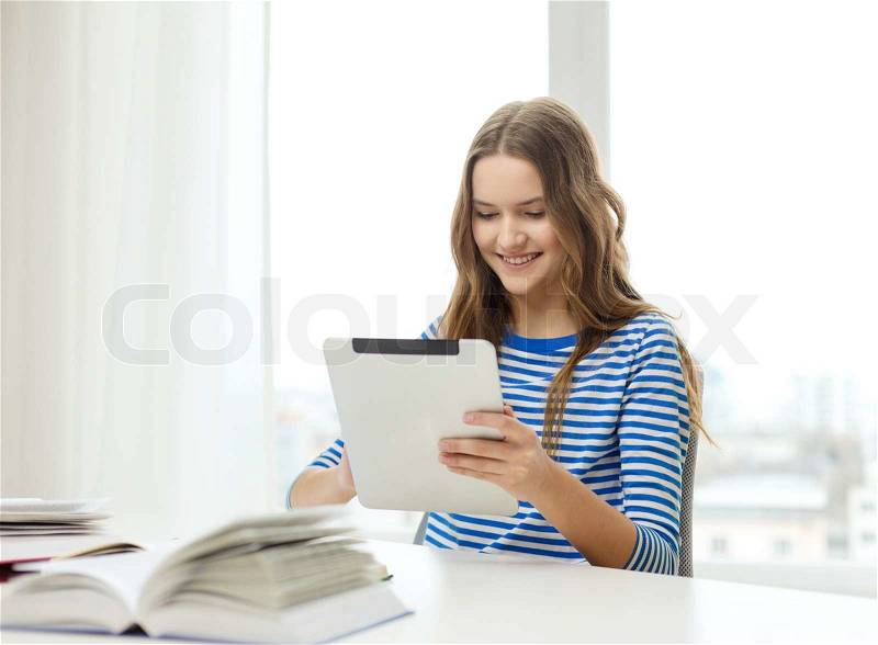 Education, technology and home concept - happy smiling student girl with tablet pc computer and books at home, stock photo