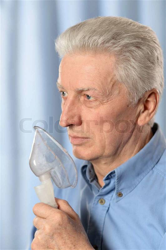 Close-up portrait of an elder man making inhalation on blue background, stock photo