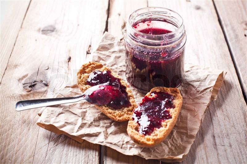 Black currant jam in glass jar and crackers on rustic wooden board, stock photo