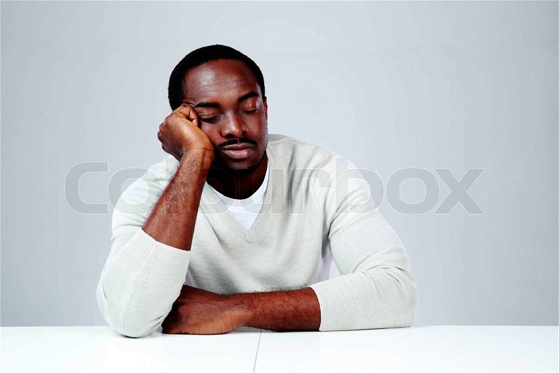 Portrait of african man sleaping at his workplace on gray background, stock photo