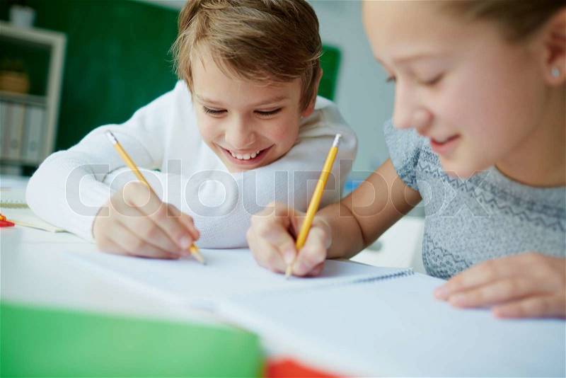 Portrait of cute schoolboy drawing at lesson with his classmate near by, stock photo