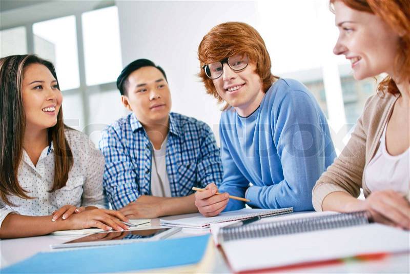 Company of smart groupmates sitting at lesson, guy in eyeglasses looking at camera, stock photo