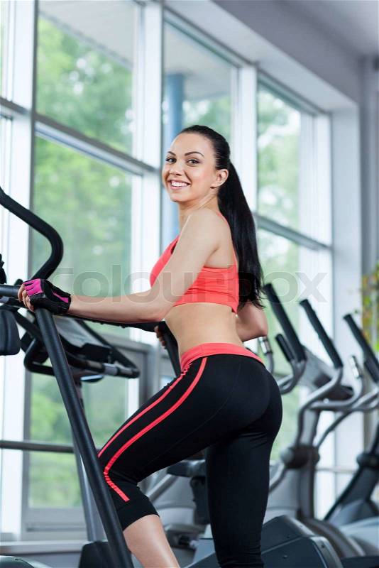 Woman doing legs exercise on stair steppers machine, young girl smile in gym fitness center, stock photo