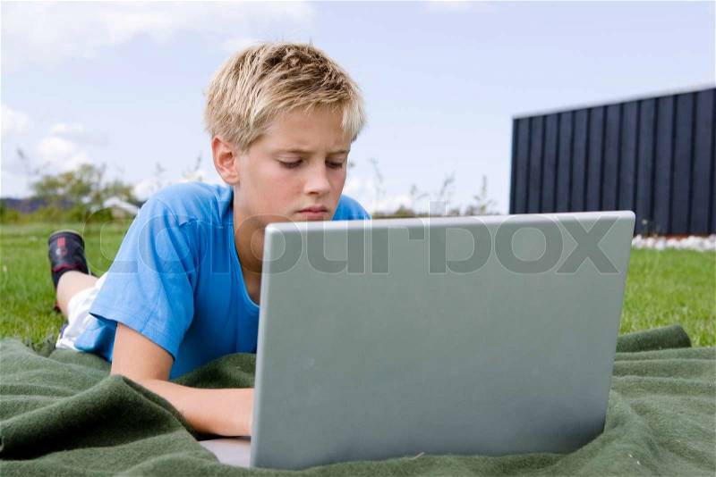 A caucasian boy browsing on his laptop in the garden, stock photo