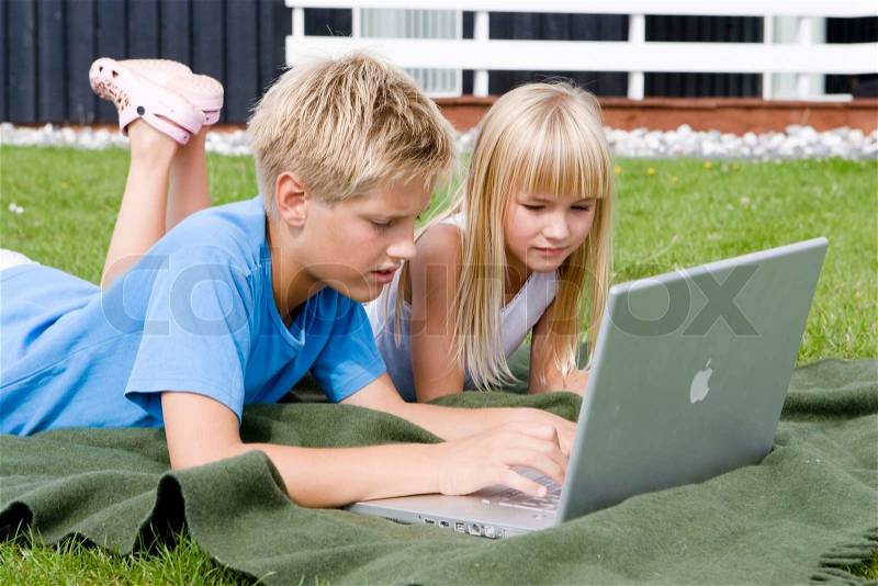 A brother and sister playing with their laptop computer in the garden, stock photo