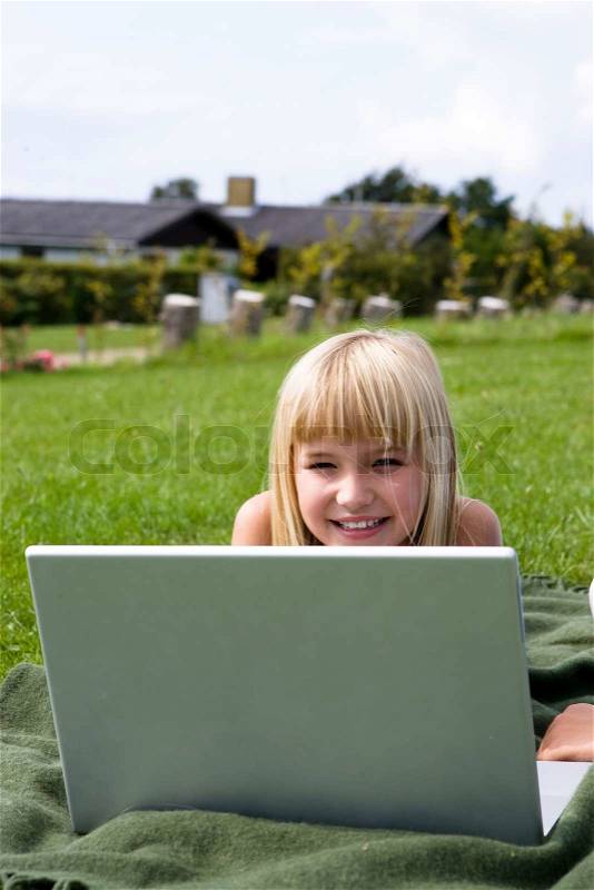 A smiling girl in the garden with her laptop, stock photo