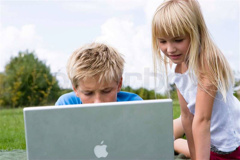 A brother and sister playing with their laptop computer in the garden, stock photo