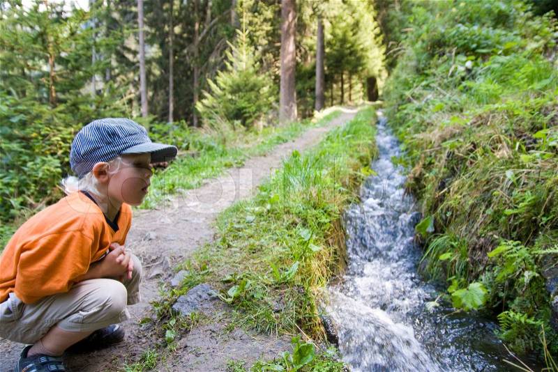 A young boy looking at a water stream along a hiking trail in Tyrol, stock photo