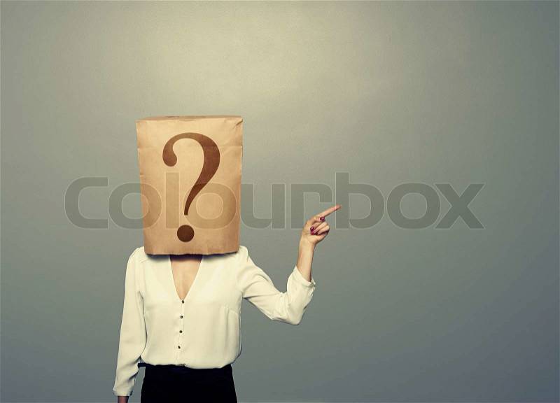 Woman with paper bag pointing at something over dark background, stock photo