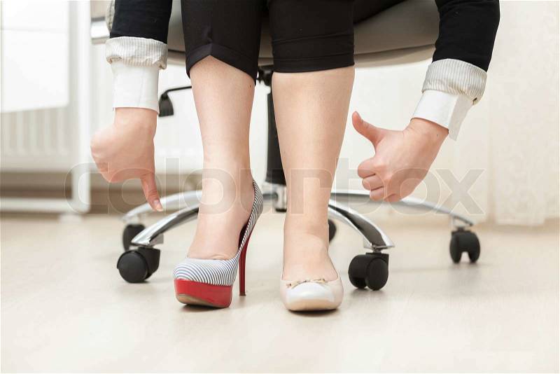 Closeup photo of woman wearing high heel shoe and ballet flat holding thumbs down and up, stock photo