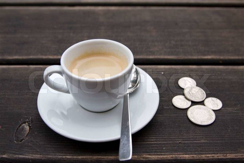 A cup of coffee and some loose change on a table, stock photo