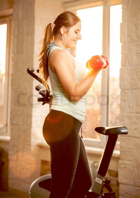 Portrait of sexy brunette woman lifting dumbbells at sport center, stock photo
