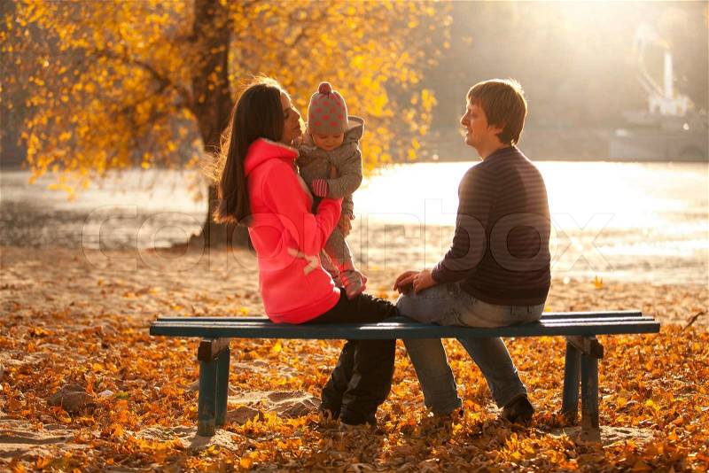 Young family having fun at autumn park on bench near river, stock photo