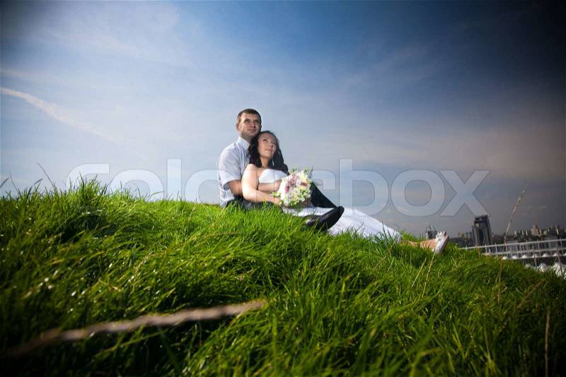 Newly married couple sitting on top of hill and looking at sky, stock photo