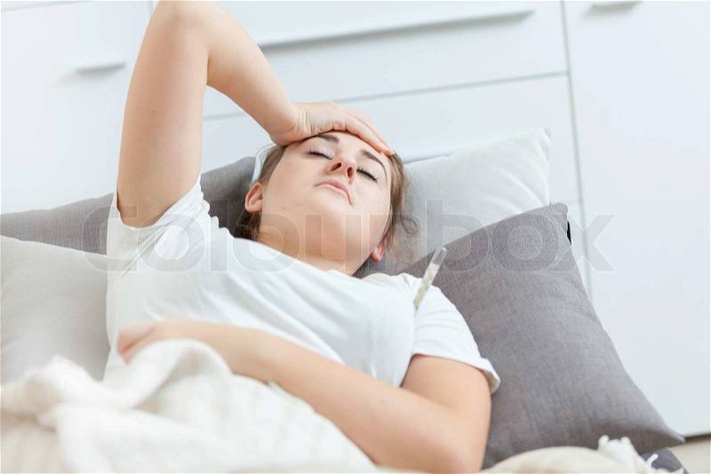 Closeup portrait of sick woman lying in bed and holding hand on head, stock photo
