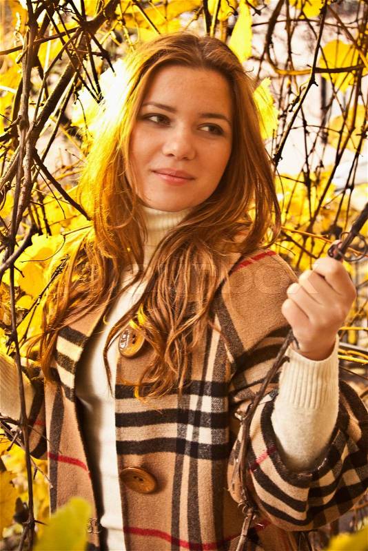 Closeup portrait of beautiful redhead woman in autumn park under tree with yellow leaves, stock photo