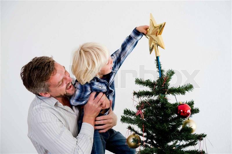 A father and his son putting the star on top of the Christmas tree, stock photo