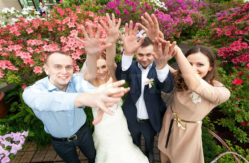 Portrait of just married couple with friends holding hands up at park, stock photo