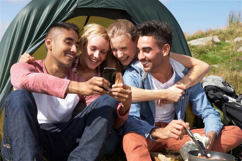 Group Of Young People Checking Mobile Phone On Camping Trip, stock photo