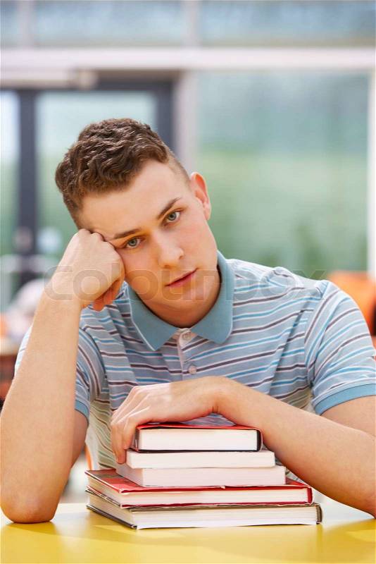Unhappy Male Student Studying In Classroom With Books, stock photo