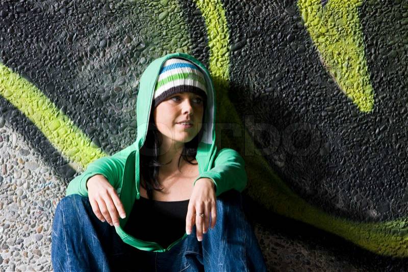 A youing woman with a green hoodie rests in a pavement, stock photo