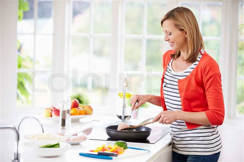 Woman Standing At Hob Preparing Meal In Kitchen, stock photo